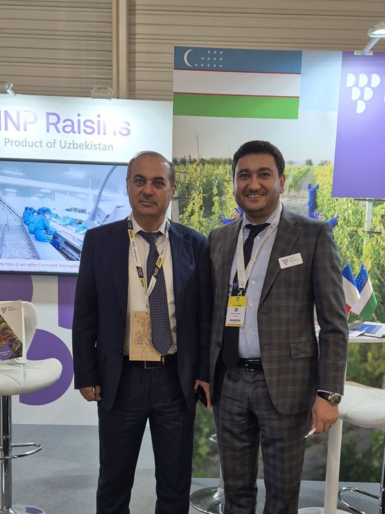Two NNP Raisins colleagues at the stand at SIAL Paris 2024, the Uzbek flag beside them.